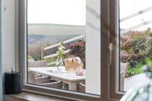 Een zithoek met rieten meubels, een tafel met een glazen vaas, en uitzicht op een natuurlandschap door een raam.