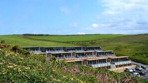 A modern hotel with a flat roof, multiple balconies, and a parking area. - 2 Bed in Watergate Bay (oc-b584340) (Tregurrian)