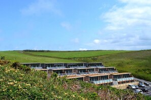 A modern hotel with a flat roof, multiple balconies, and a parking area. - 2 Bed in Watergate Bay (oc-b584340) (Tregurrian)
