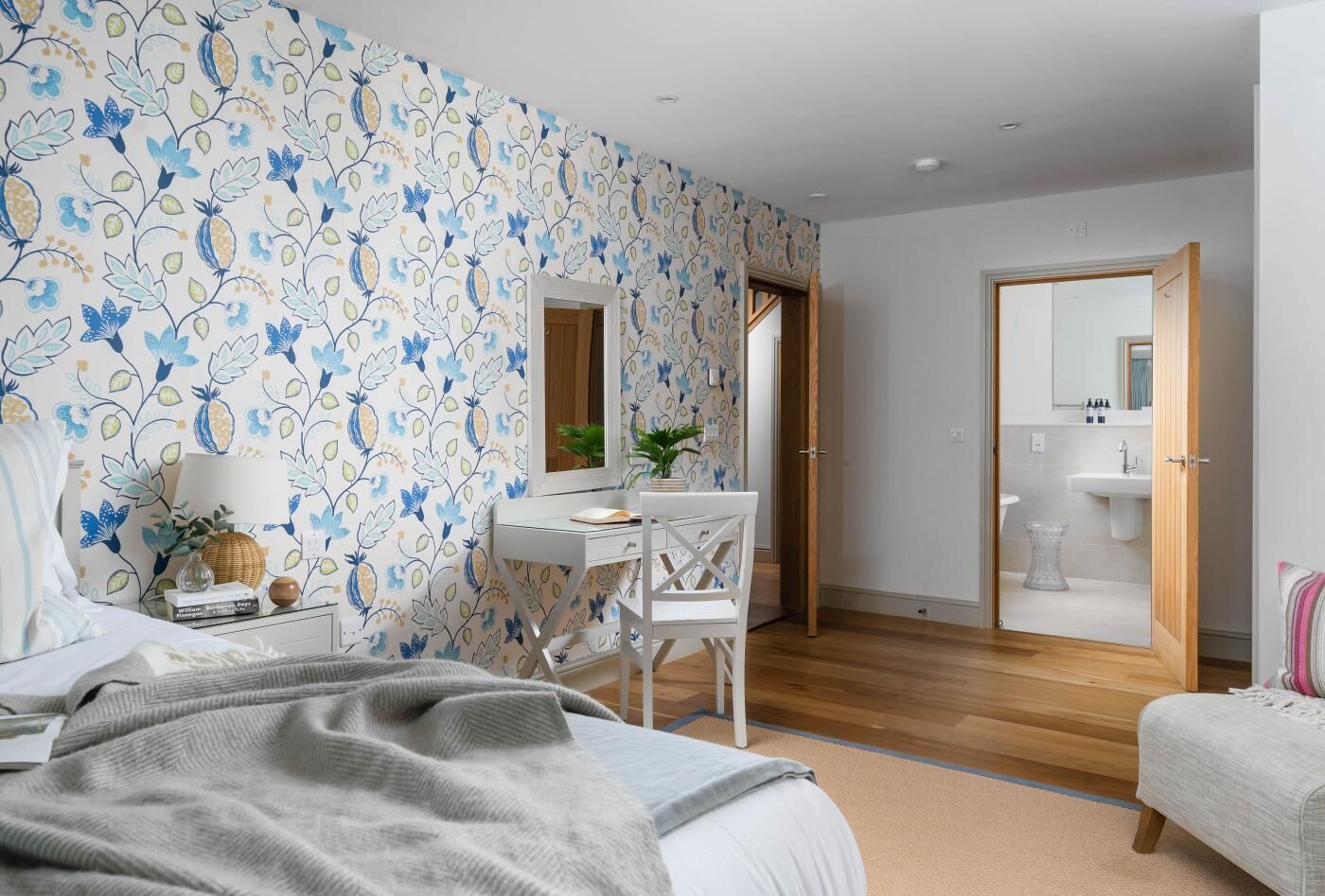 Ein Schlafzimmer mit Bett, Schreibtisch, Stuhl, Nachttisch, Spiegel und angrenzendem Badezimmer.
