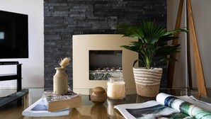 A modern living room with a fireplace, a television, a plant, and a table with books and candles. - 2 Bed in Watergate Bay (oc-b584340) (Tregurrian)
