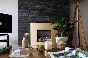 A modern living room with a fireplace, a television, a plant, and a table with books and candles. - 2 Bed in Watergate Bay (oc-b584340) (Tregurrian)
