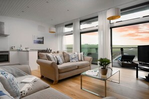 A modern living room with a sofa, a glass coffee table, and a view of the outdoors. - 2 Bed in Watergate Bay (oc-b584340) (Tregurrian)
