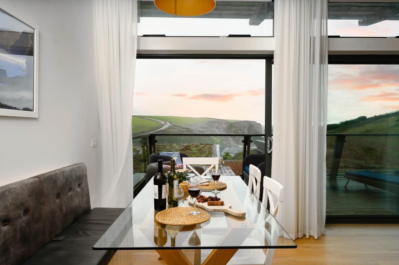 A dining area with a glass table and chairs, a sofa, and a scenic view through large windows.
