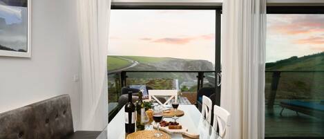 Un comedor con mesa y sillas de vidrio, un sofá y una vista panorámica a través de amplios ventanales.