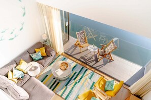 Ein Balkon mit einer Couch, Stühlen, einem kleinen Tisch und einem Glasgeländer mit Blick auf einen Pool.