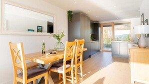 A dining area with a wooden table and chairs, a large mirror, and a view of the outdoors. - 3 Bed in Hayle (oc-b635644) (Hele)