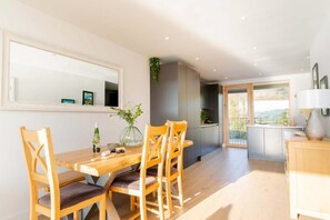 Ein Essbereich mit Holztisch und Stühlen, einem großen Spiegel und Blick ins Freie.