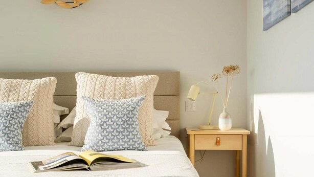 A neatly made bed with a book, a bedside lamp, and a small wooden nightstand with a vase. - 3 Bed in Hayle (oc-b635644) (Hele)