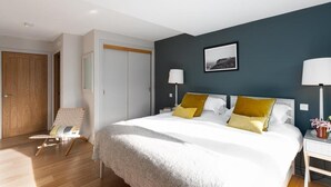 A hotel room with a bed, bedside lamps, a chair, a wardrobe, and a framed picture on the wall. - 2 Bed in Watergate Bay (oc-b584354) (Tregurrian)