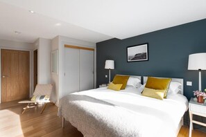 Ein Hotelzimmer mit Bett, Nachttischlampen, einem Sessel, einem Kleiderschrank und einem gerahmten Bild an der Wand.