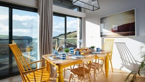 A dining area with a table set for four, large windows with a view, and a modern pendant light. - 2 Bed in Watergate Bay (oc-b584354) (Tregurrian)