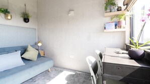 A modern living room with a blue sofa, a desk with a printer, and a window with a view of the outside. - 3 Bed in Downderry (oc-b652220) (Downderry)