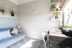 Uma sala de estar moderna com um sofá azul, uma mesa de escritório com uma impressora e uma janela com vista para o exterior.