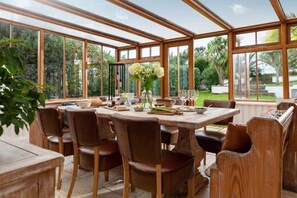 Ein Wintergarten mit einem Holztisch, gedeckt für ein Essen, umgeben von Stühlen.