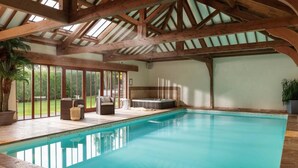 An indoor swimming pool with a wooden ceiling, a hot tub, and seating area with a view of the outdoors. - 5 Bed in Holywell Bay (oc-b614951) (Cubert)