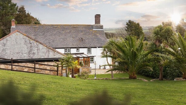 A traditional white house with a stone roof, a stone wall, and a fenced yard. - 5 Bed in Holywell Bay (oc-b614951) (Cubert)