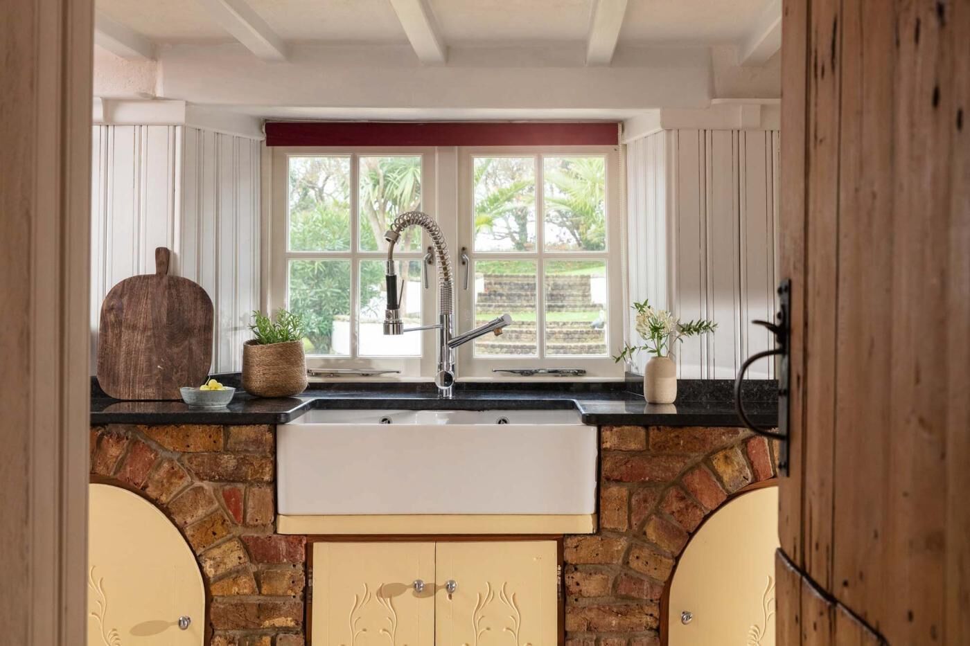 Uma cozinha com painel de backsplash de pedra, uma pia branca e uma janela com vista para o verde.