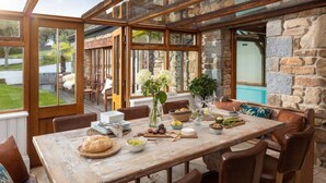 An outdoor dining area with a stone wall, wooden table, and chairs. - 5 Bed in Holywell Bay (oc-b614951) (Cubert)