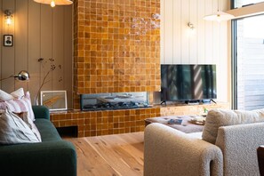 A modern living room with a fireplace, a television, and a cozy seating area. - 3 Bed in Watergate Bay (oc-b597580) (Tregurrian)