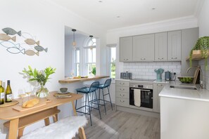 Eine moderne Küche mit einem Holztisch, Barhocker, einem eingebauten Backofen und einem Fenster mit Blick auf den Garten.