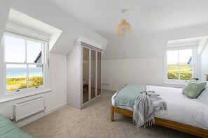 Ein Schlafzimmer mit einem Bett, zwei Fenstern, einem Kleiderschrank und einer Pendelleuchte.