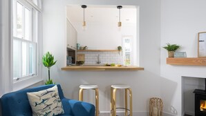 A modern living room with a blue sofa, two stools, a fireplace, and a kitchen visible through an archway. - 2 Bed in Fistral (oc-b625209) (Newquay)