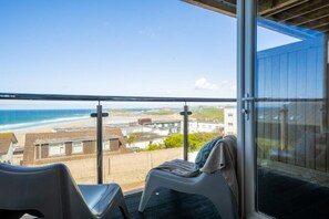 A balcony with a view of the beach and ocean, two plastic chairs, and a glass door. - 3 Bed in Fistral (oc-b595429) (Newquay)
