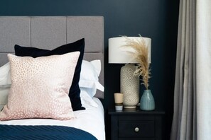 Una cama bien hecha con un cojín estampado y una lámpara decorativa a un lado.