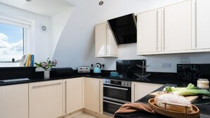 A modern kitchen with a black countertop, white cabinets, and a window with a view. - 3 Bed in Fistral (oc-b595429) (Newquay)