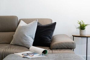 Ein Sofa mit zwei Kissen, ein kleiner Tisch mit einer Pflanze und eine Zeitschrift mit Gläsern darauf.
