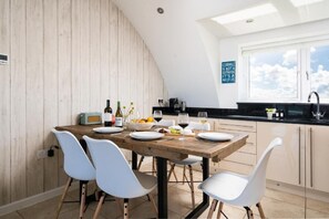 Ein Essbereich mit einem Holztisch, weißen Stühlen und einer Küche im Hintergrund.