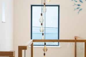 A modern interior with a wooden staircase, a hanging light fixture, and a window with a view. - 5 Bed in Carbis Bay (oc-b623959) (Carbis Bay)