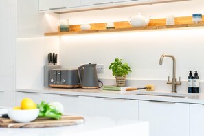 A modern kitchen with a built-in toaster, a kettle, a sink, and a countertop with a bowl of lemons and a cutting board. - 5 Bed in Carbis Bay (oc-b623959) (Carbis Bay)