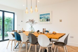 A dining area with a wooden table, white and gray chairs, hanging light fixtures, and a framed picture on the wall. - 5 Bed in Carbis Bay (oc-b623959) (Carbis Bay)