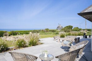 An outdoor patio with wicker furniture, a small table with a vase, and a view of the ocean. - 5 Bed in Sennen (oc-b622152) (Trewolla)