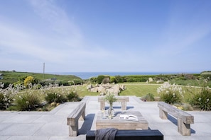 A patio with a view of the sea, stone benches, and a grassy area. - 5 Bed in Sennen (oc-b622152) (Trewolla)
