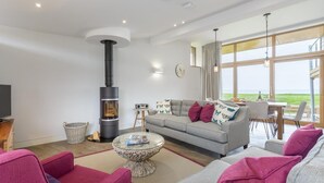 A modern living room with a fireplace, a sofa set, a coffee table, and a view of the outdoors. - 3 Bed in Widemouth Bay (oc-b584375) (Widemouth Bay)