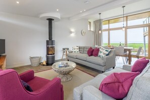 A modern living room with a fireplace, a sofa set, a coffee table, and a view of the outdoors. - 3 Bed in Widemouth Bay (oc-b584375) (Widemouth Bay)