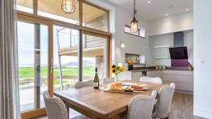 A dining area with a view of a golf course, a kitchen with modern appliances, and wicker chairs. - 3 Bed in Widemouth Bay (oc-b584375) (Widemouth Bay)