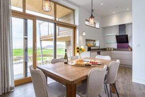 A dining area with a view of a golf course, a kitchen with modern appliances, and wicker chairs. - 3 Bed in Widemouth Bay (oc-b584375) (Widemouth Bay)