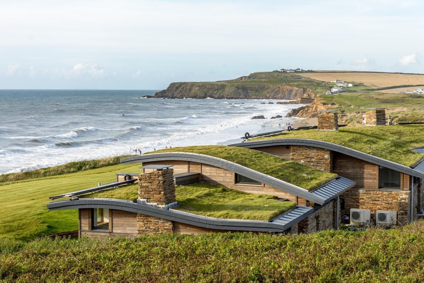 A coastal property with a curved roof structure, stone walls, and a grassy roof.