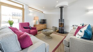 A modern living room with a sofa, armchair, and a fireplace. - 3 Bed in Widemouth Bay (oc-b584375) (Widemouth Bay)