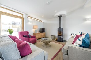 A modern living room with a sofa, armchair, and a fireplace. - 3 Bed in Widemouth Bay (oc-b584375) (Widemouth Bay)