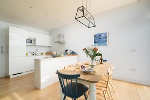 Eine moderne Küche mit weißen Schränken, einer zentralen Kochinsel und einem Essbereich mit Holztisch und Stühlen.
