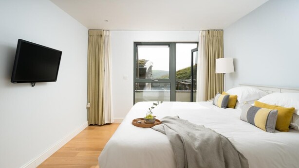 A hotel room with a bed, a television, a window with curtains, and a view of a bridge. - 2 Bed in Watergate Bay (oc-b584380) (Tregurrian)