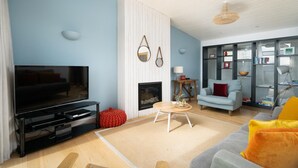 A modern living room with a flat-screen TV, a fireplace, a sofa, and a bookshelf. - 2 Bed in Watergate Bay (oc-b584380) (Tregurrian)