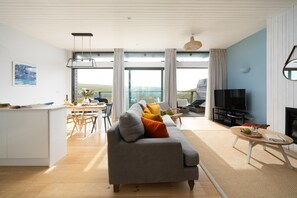 A modern living room with a sofa, television, and a dining area with chairs and a table. - 2 Bed in Watergate Bay (oc-b584380) (Tregurrian)