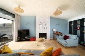 A living room with a TV, sofa, fireplace, and a bookshelf. - 2 Bed in Watergate Bay (oc-b584380) (Tregurrian)