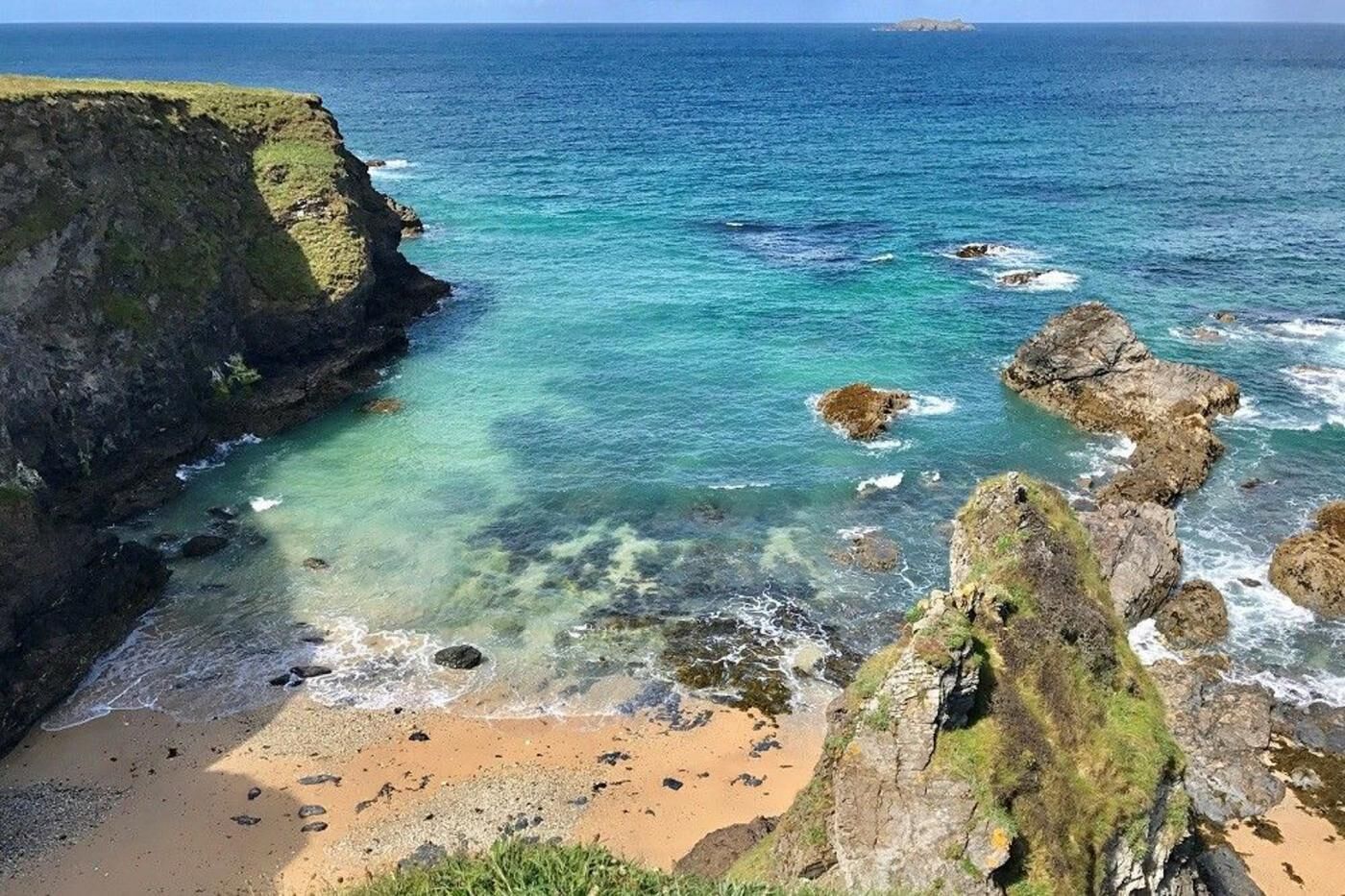 A coastal landscape with a sandy beach, rocky outcrops, and clear blue waters.